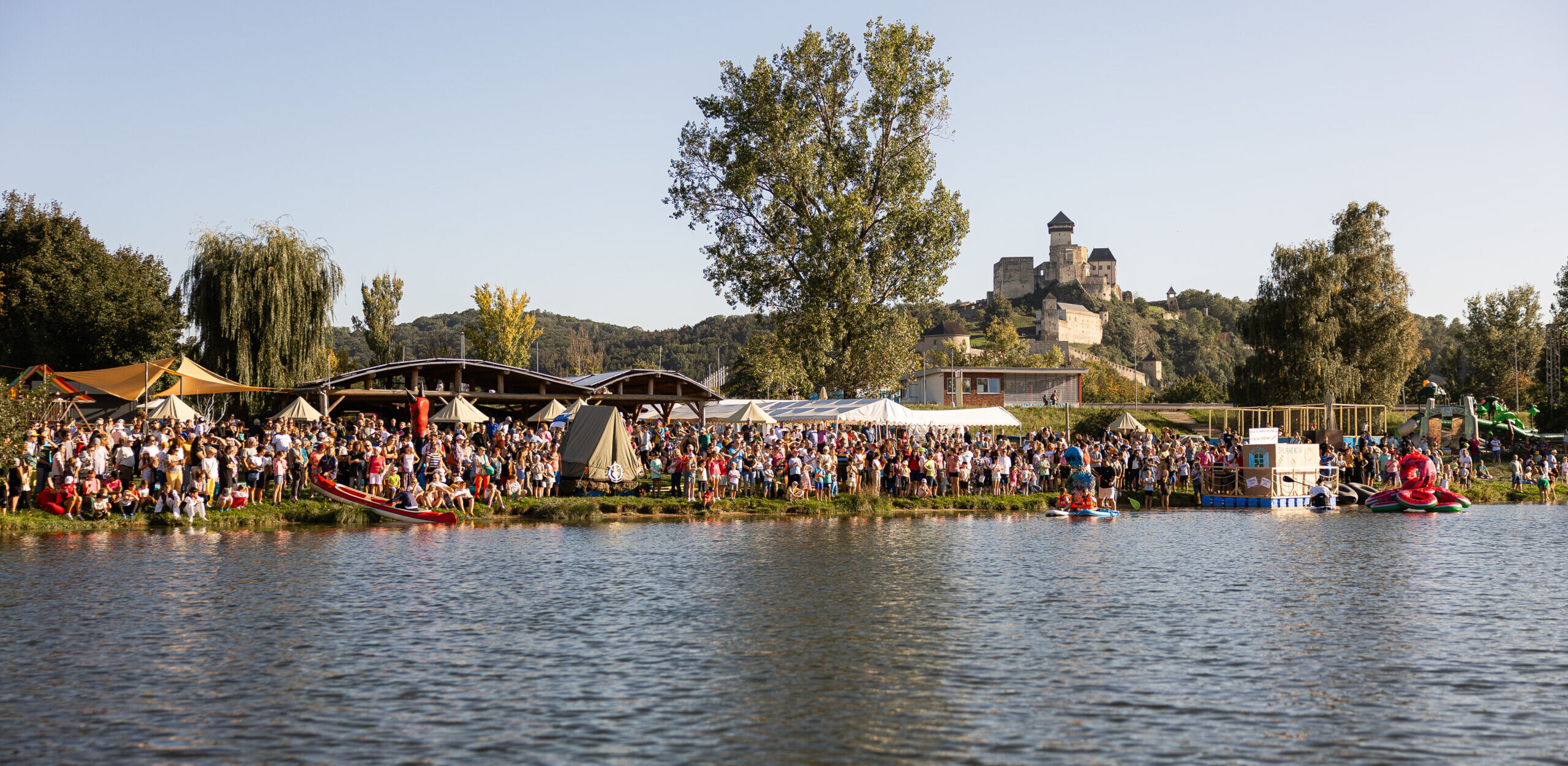 Crowd gathered along a riverbank with a castle in the distance.