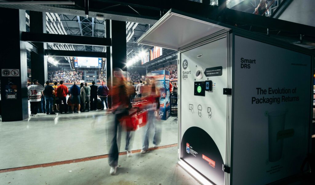 Visitors passing an indoor cup-return kiosk at a crowded hockey event.