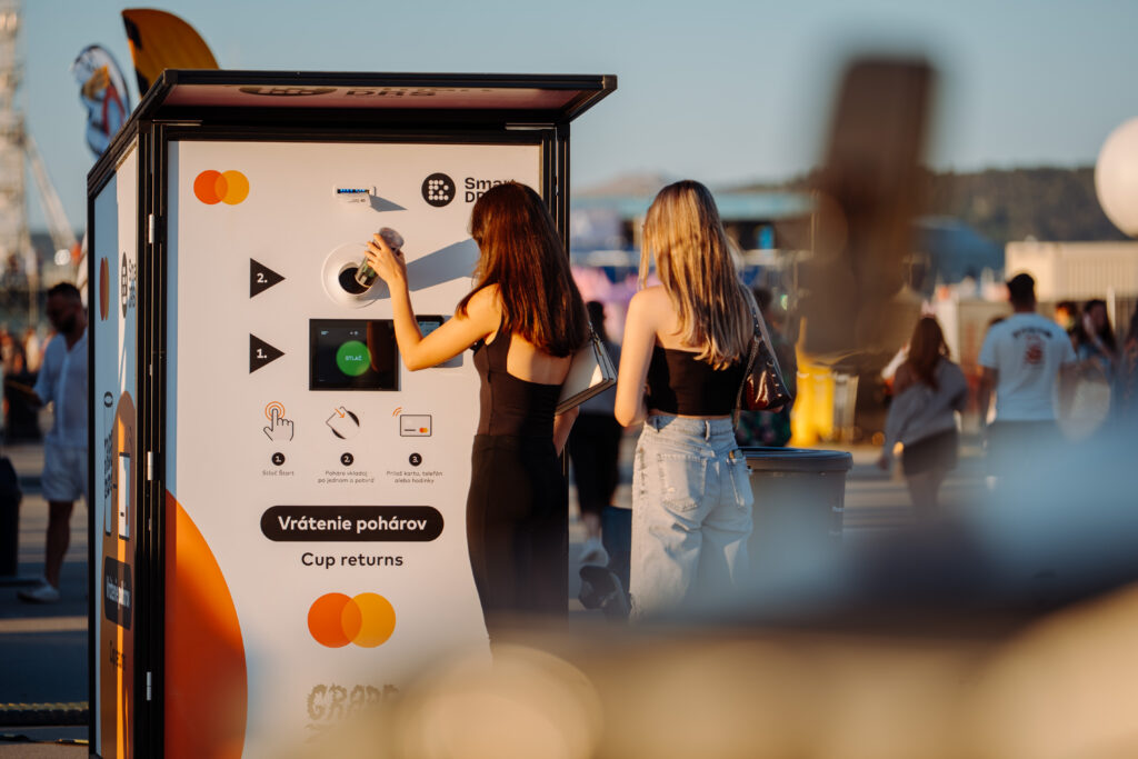 Two festival visitors using a Smart DRS reusable cup return station at an outdoor event