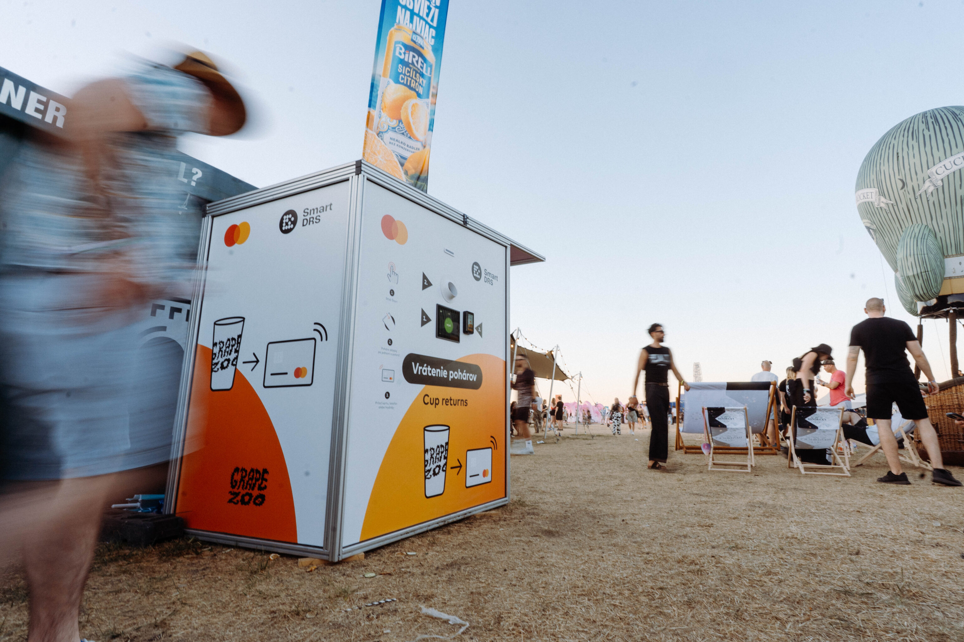 Smart DRS reusable cup return station with festival visitors and a Ferris wheel in the background