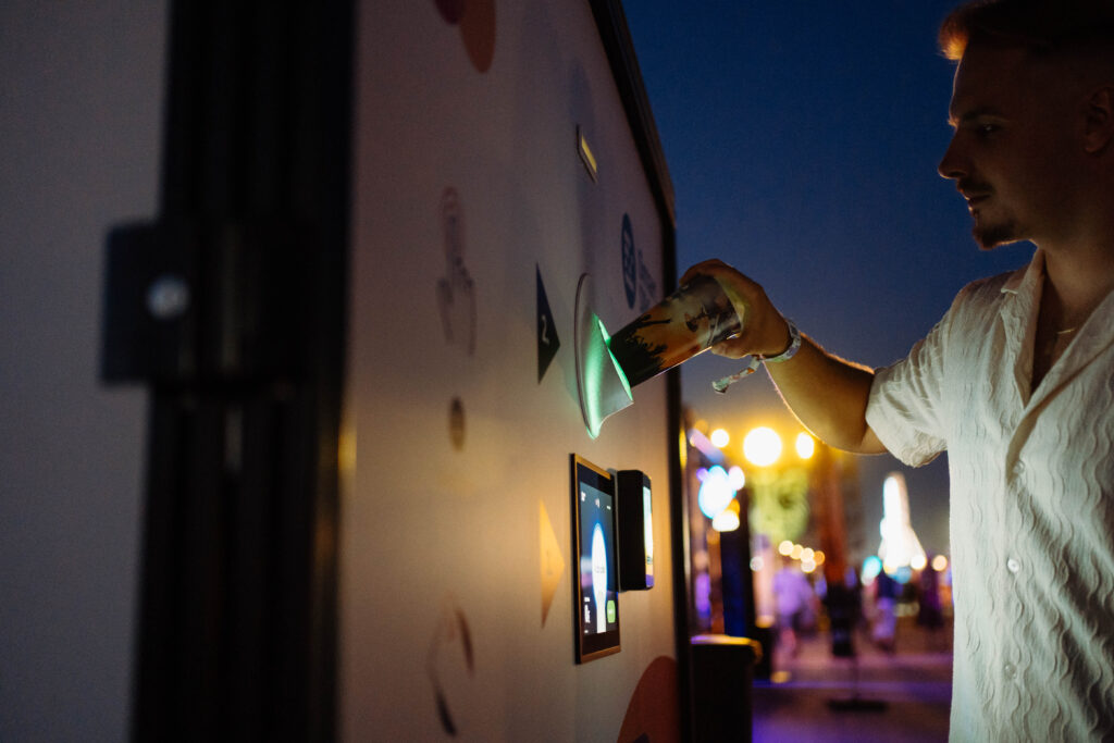 Visitor inserting a reusable cup into a Smart DRS return station at Grape Festival 2026 at night