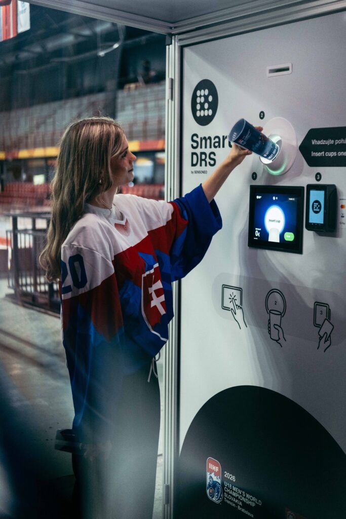Visitor in a Slovak hockey jersey returning a reusable cup through a Smart DRS station