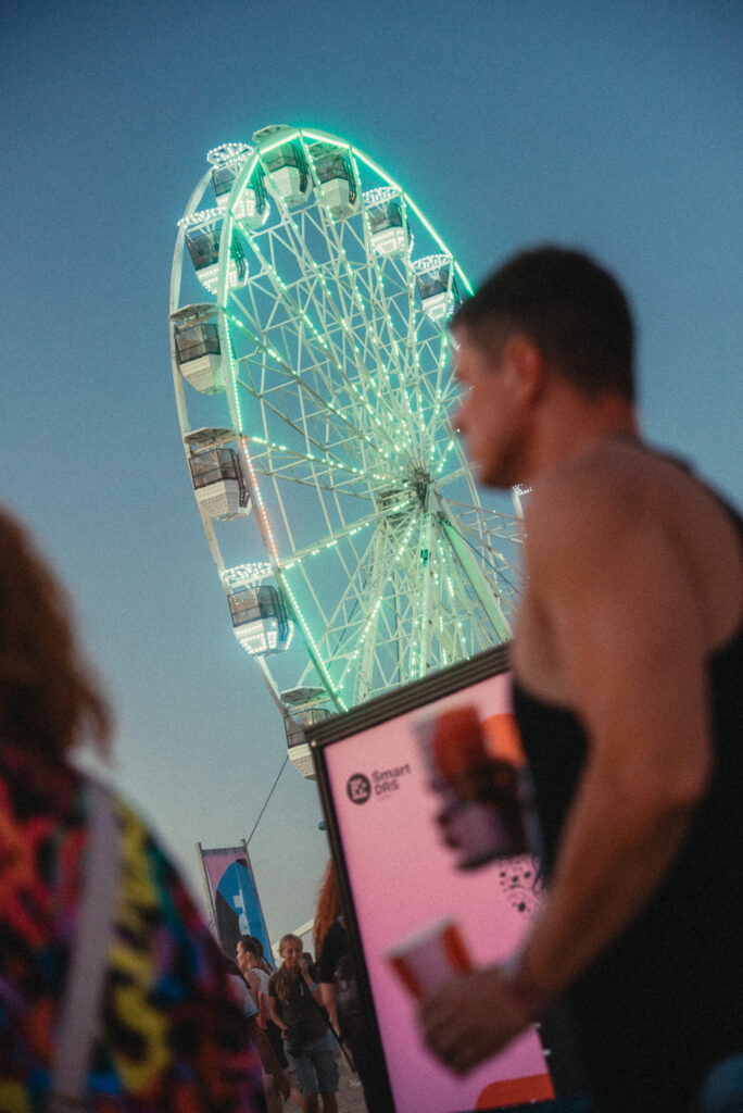 Návštevník pri poháromatoch Smart DRS na festivale LOVESTREAM 2026 s festivalovým kolesom v pozadí.